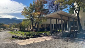Un edificio con un portico coperto, circondato da alberi e un vialetto sterrato.