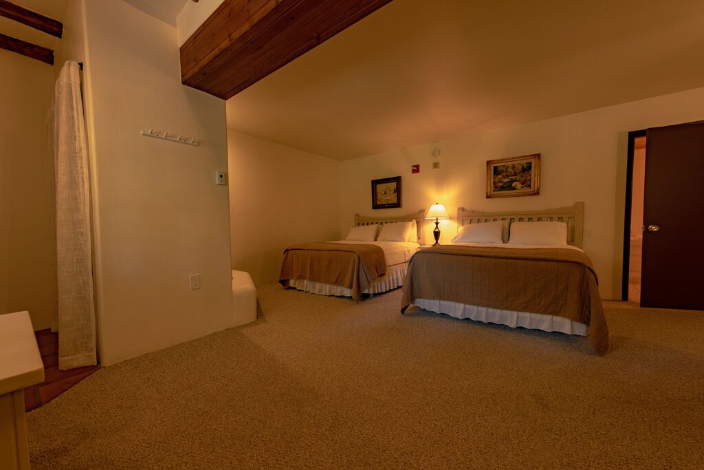 A bedroom with two beds, a wooden ceiling, a door, and a small table.