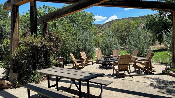 Une terrasse extérieure avec des tables et des chaises en bois, entourée de verdure et offrant une vue sur un paysage montagneux.