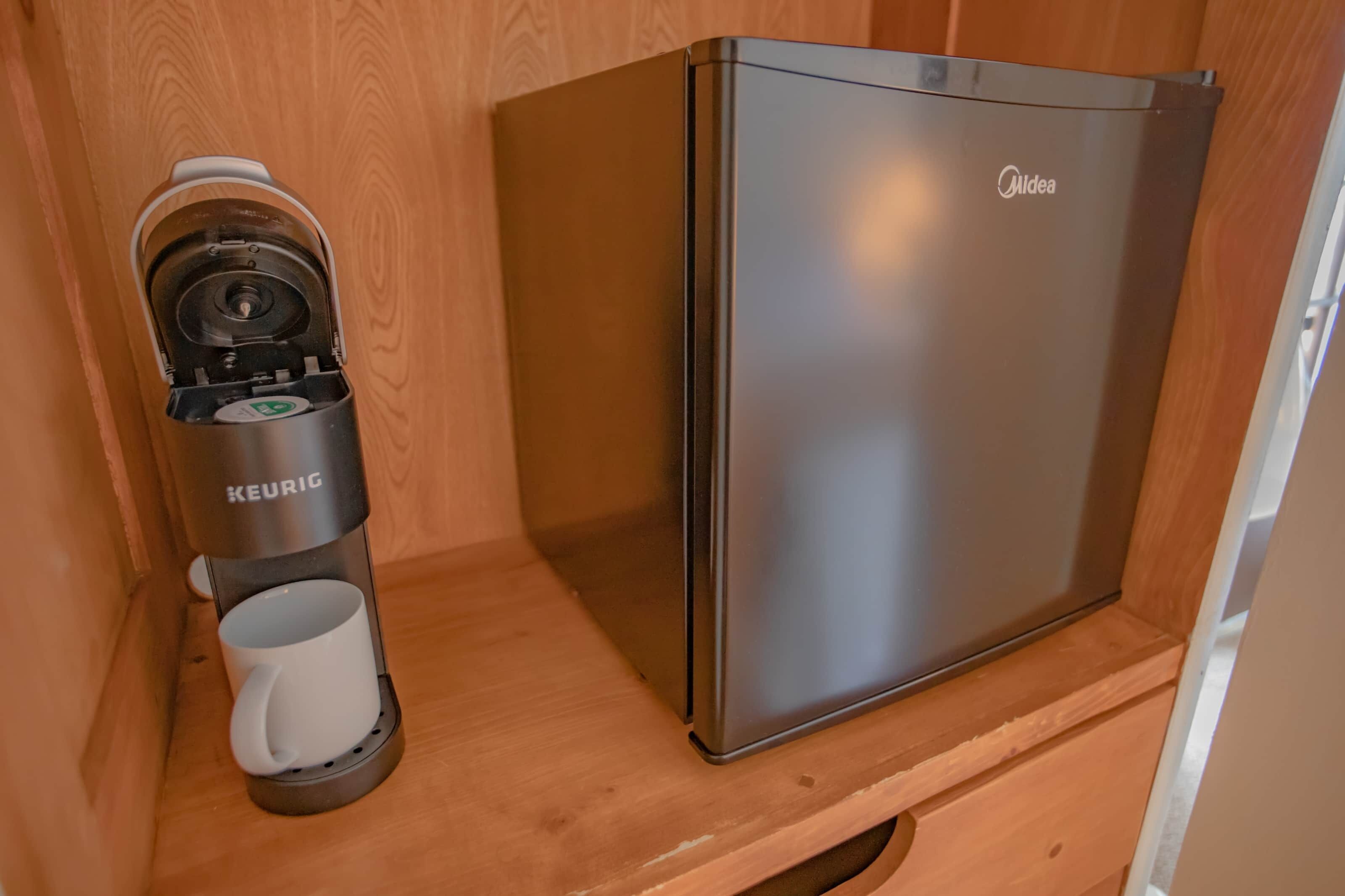 Un réfrigérateur Midea élégant, en acier inoxydable, doté d’une machine à café Keurig intégrée, posé sur une étagère en bois.