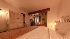 Une chambre avec un grand lit, des poutres en bois, une cloison en verre et une vue sur une autre pièce.