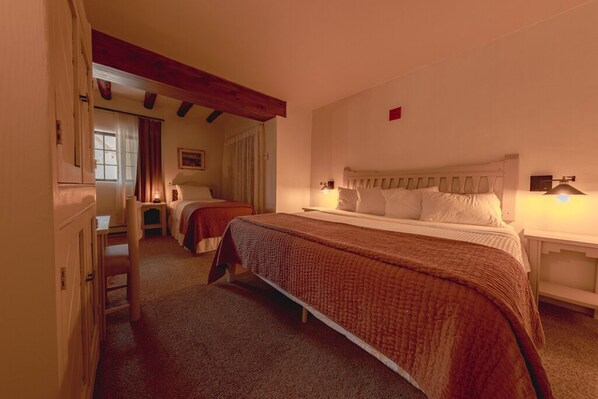 Classic bedroom with a large bed, wooden beams, and a bedside table with lamps.
