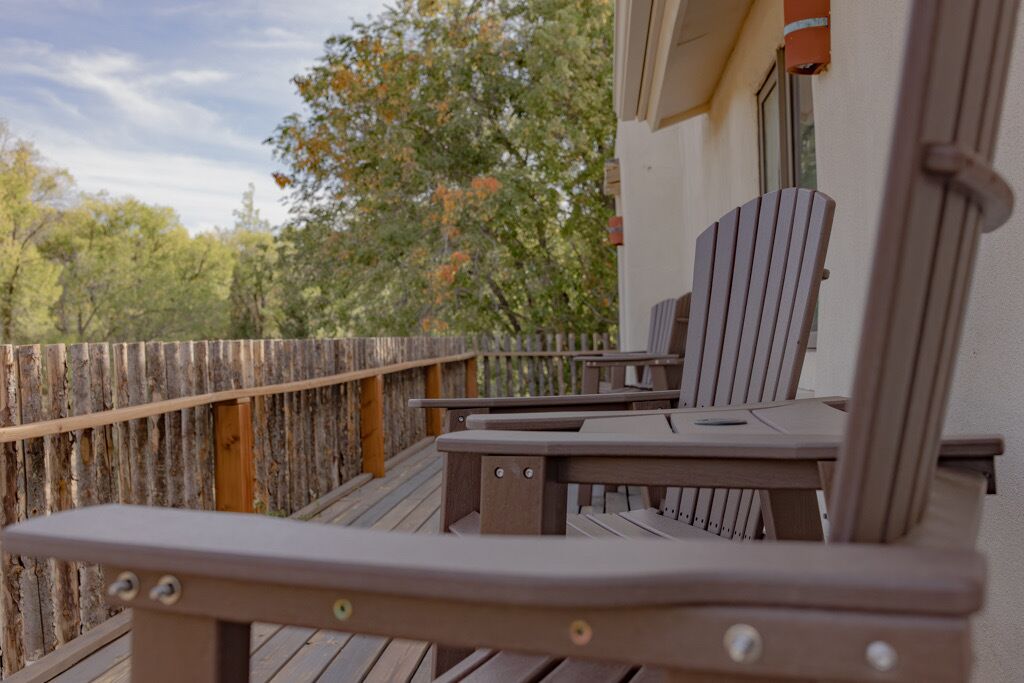 A wooden deck with a table and chairs, a wooden fence, and trees in the background.