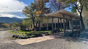A building with a covered patio, a gravel pathway, and trees with autumn foliage. - Queen room w/ gas fireplace - 16 (Taos County)