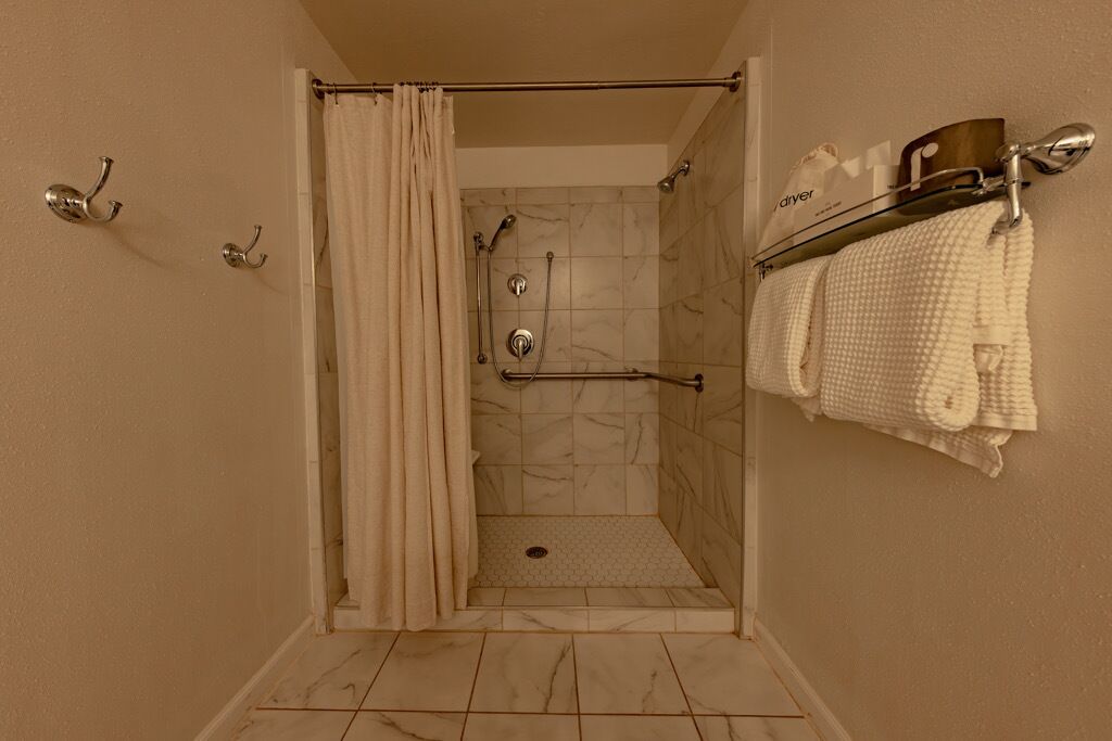 A shower area with a marble floor, a towel rack with towels, and a shower curtain.