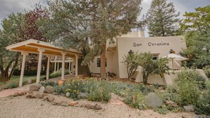 Un edificio con el nombre 'San Geronimo' en su fachada, rodeado por un jardín con diversas plantas y una estructura de pérgola.