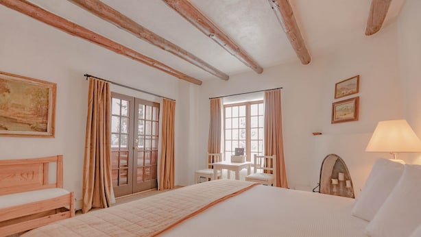 Un dormitorio con una cama grande, un banco de madera, una mesita con sillas y una lámpara.