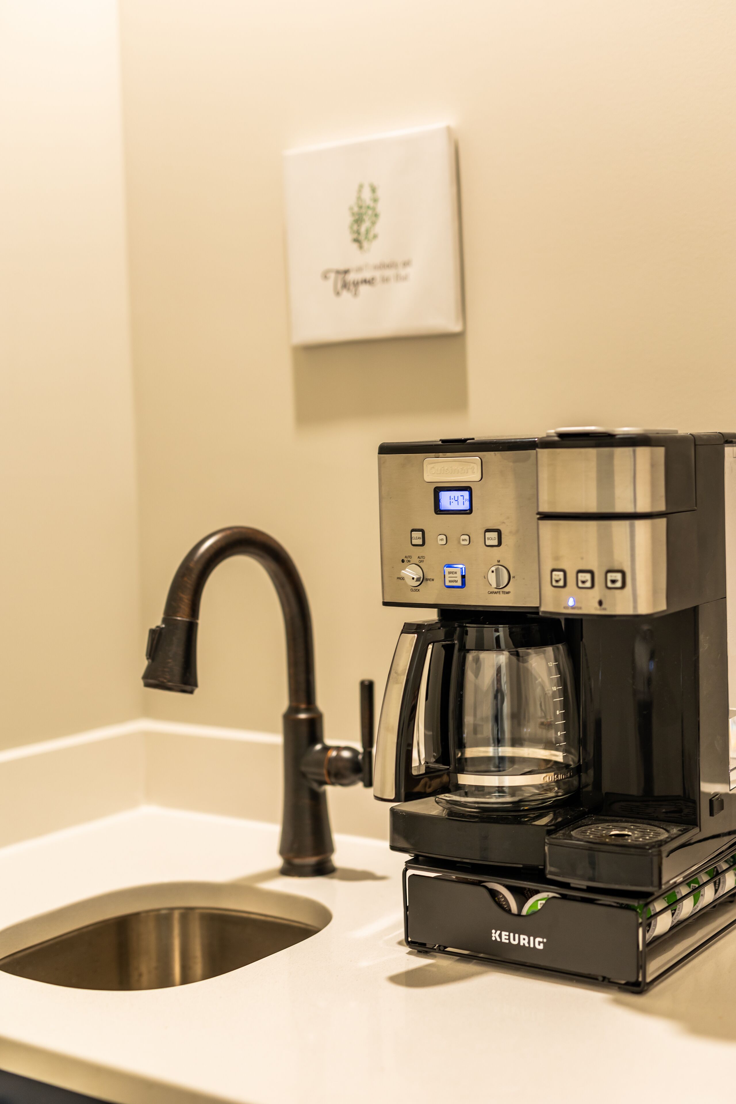 Una cafetera Keurig sobre una encimera con un lavabo y un cuadro en la pared.