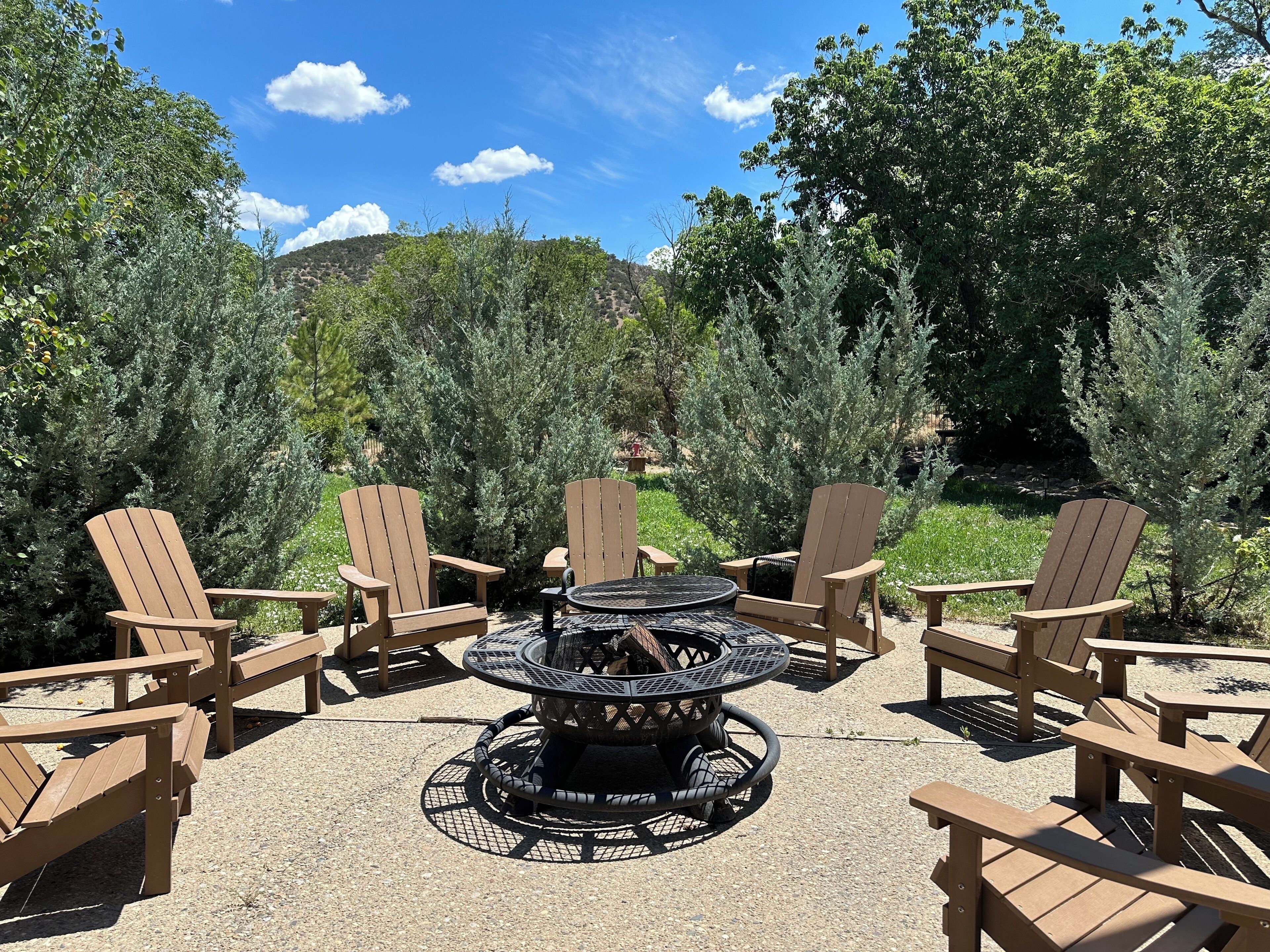 A patio area with Adirondack chairs and a circular table with a fire pit in the center.