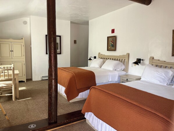 A hotel room with two beds, a wooden headboard, a nightstand with a lamp, and a desk with a chair. - Family suite w/ Mountain View - 11 (Taos County)