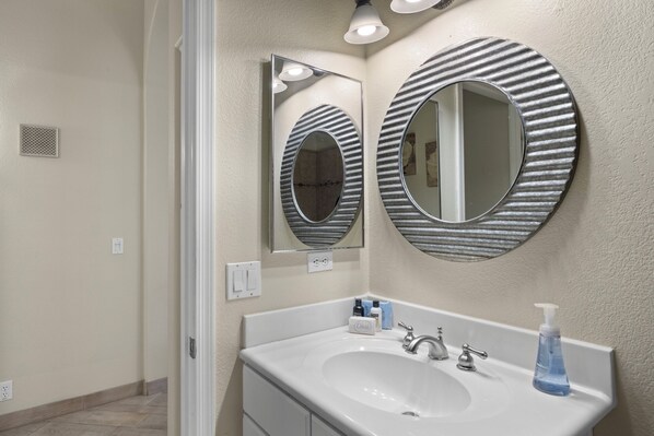 Un baño con un lavabo blanco, dos espejos de distintos diseños, un grifo y un dispensador de jabón.