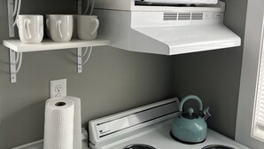 A kitchen with a white stove, a teal kettle, and a microwave on a white shelf above the stove. - Small Home in the City of Alexandria! (Alexandria)