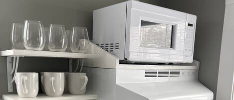 Una cocina con una estufa blanca, un hervidor celeste y un microondas sobre un estante blanco.