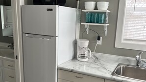 A kitchen with a white refrigerator, a marble countertop, a sink, and a window with blinds. - Small Home in the City of Alexandria! (Alexandria)