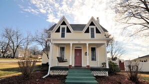 A two-story house with a front porch, a red door, and a mailbox.