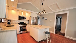 A modern kitchen with white cabinetry, stainless steel appliances, a wooden floor, and a bar stool.