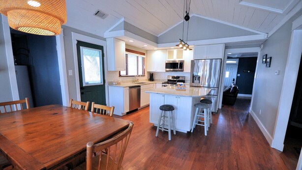 A modern kitchen with wooden flooring, white cabinetry, and a central island with stools.