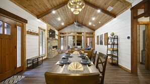 Une salle à manger spacieuse avec un plafond haut et des poutres en bois, où se trouve une grande table dressée pour six personnes, avec des bols et des assiettes.