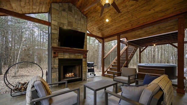 Un intérieur de chalet chaleureux avec une cheminée en pierre, des sièges confortables, un bain à remous et un escalier menant à une terrasse.