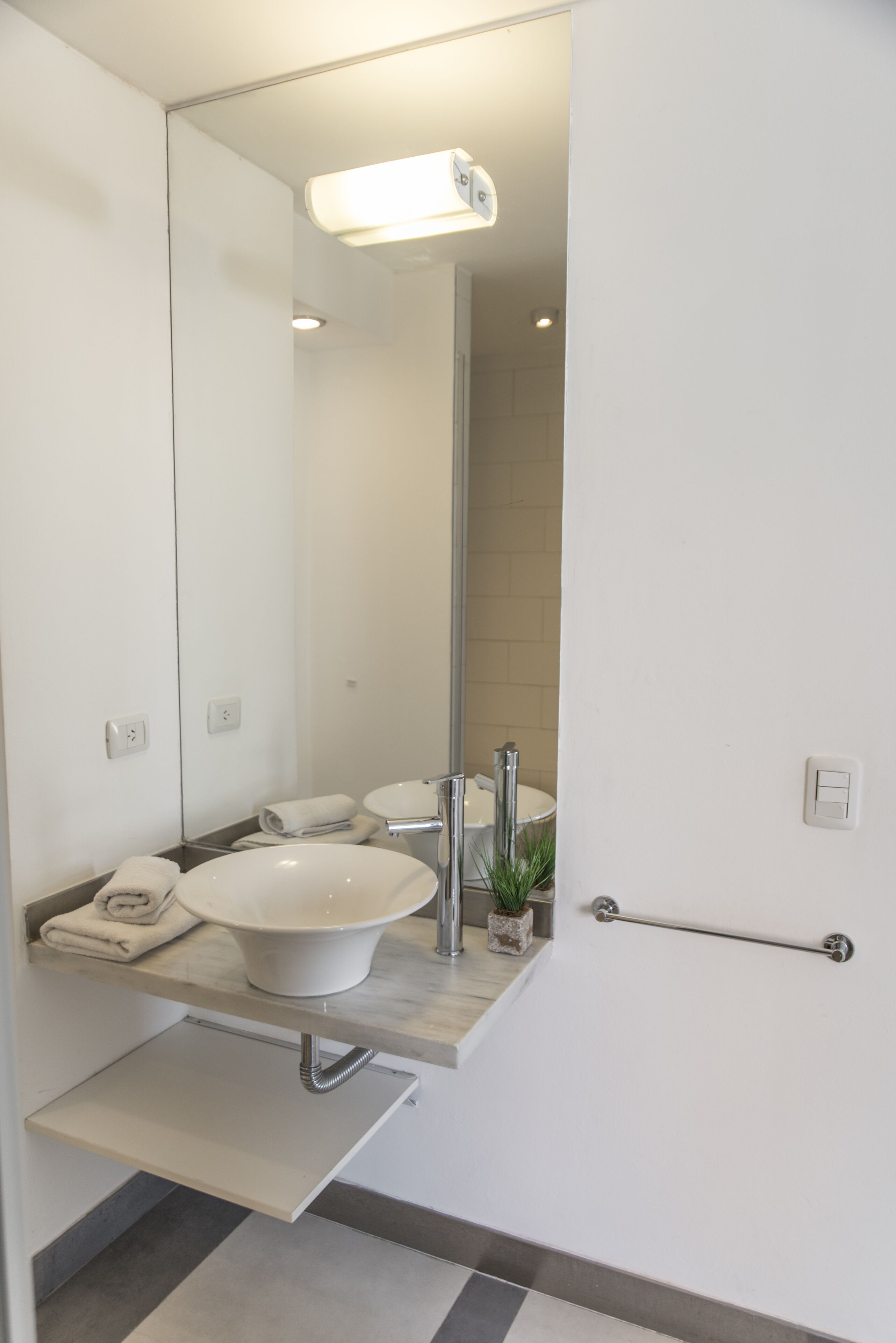 A modern bathroom with a white sink, mirror, and towel rack.
