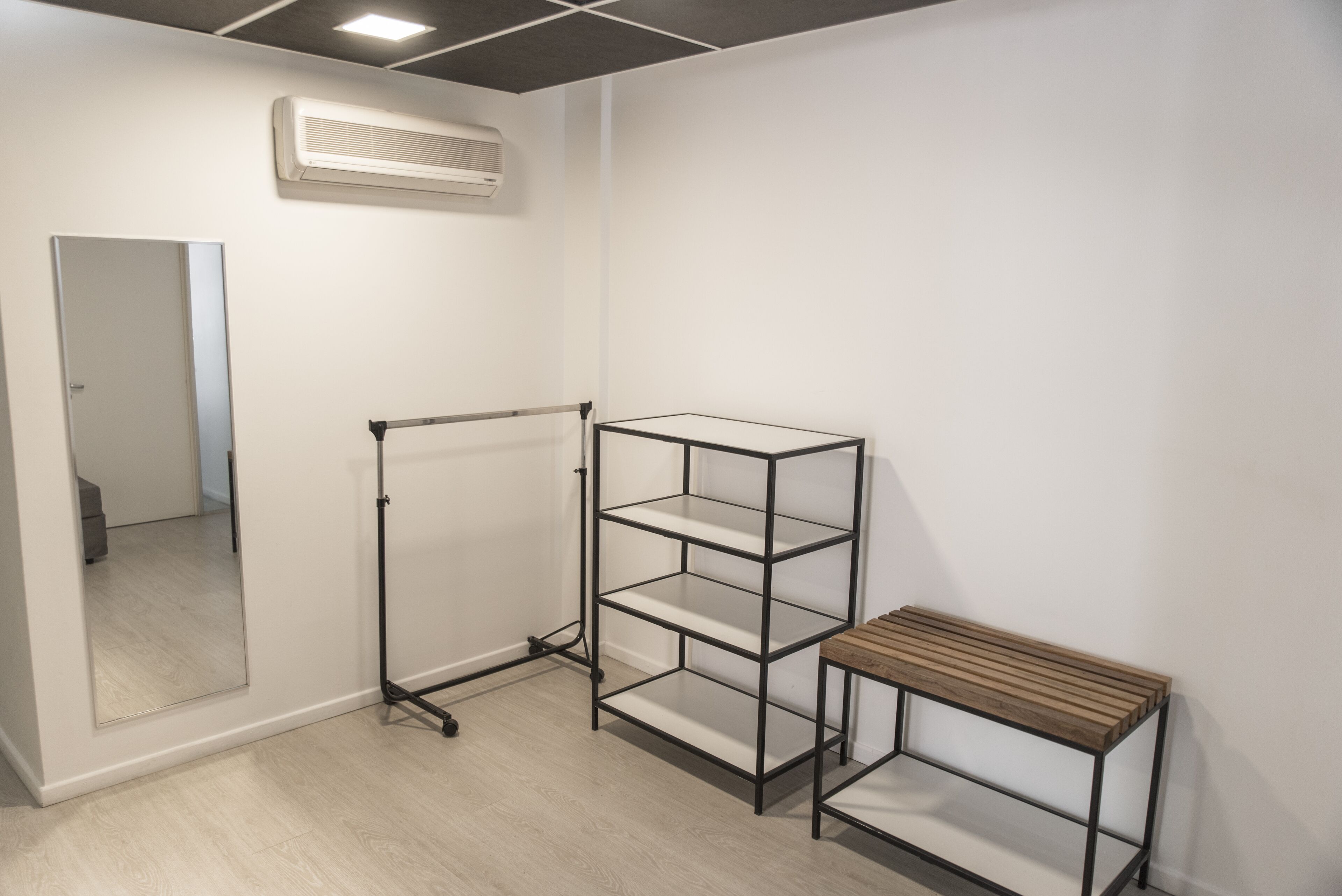 A room with a metal shelving unit, a wooden bench, and a mirror on the wall.