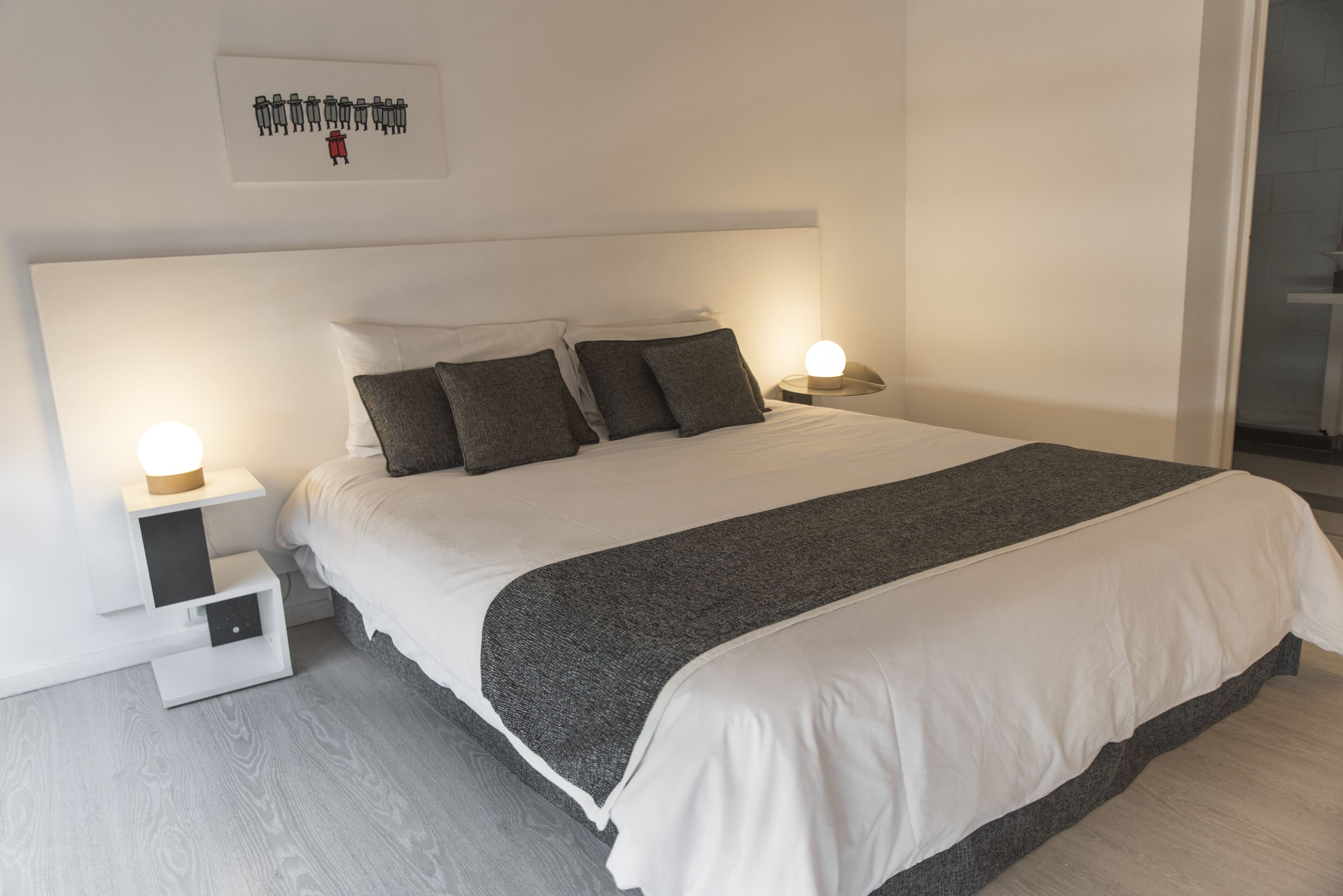 A modern bedroom with a large bed, two bedside tables with lamps, a headboard, and a wall-mounted artwork.