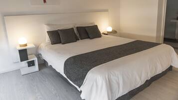 Une chambre moderne avec un grand lit, deux tables de chevet avec des lampes, une tête de lit et une œuvre d’art accrochée au mur.