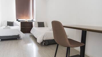 Una habitación con dos camas, una silla, una mesa y un ventanal con persianas.