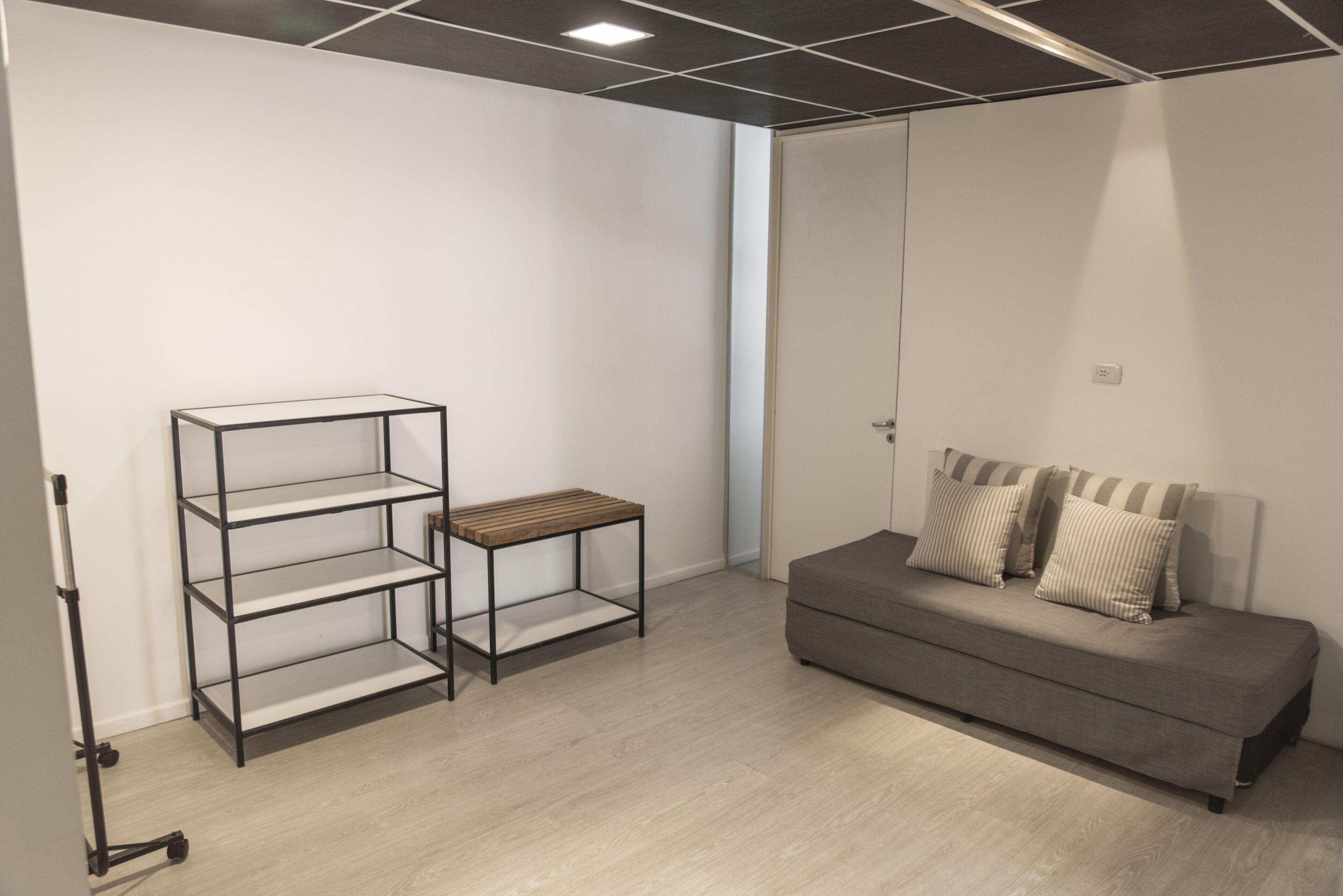 Una habitación moderna con un sofá gris, una mesita de madera y una estantería metálica.