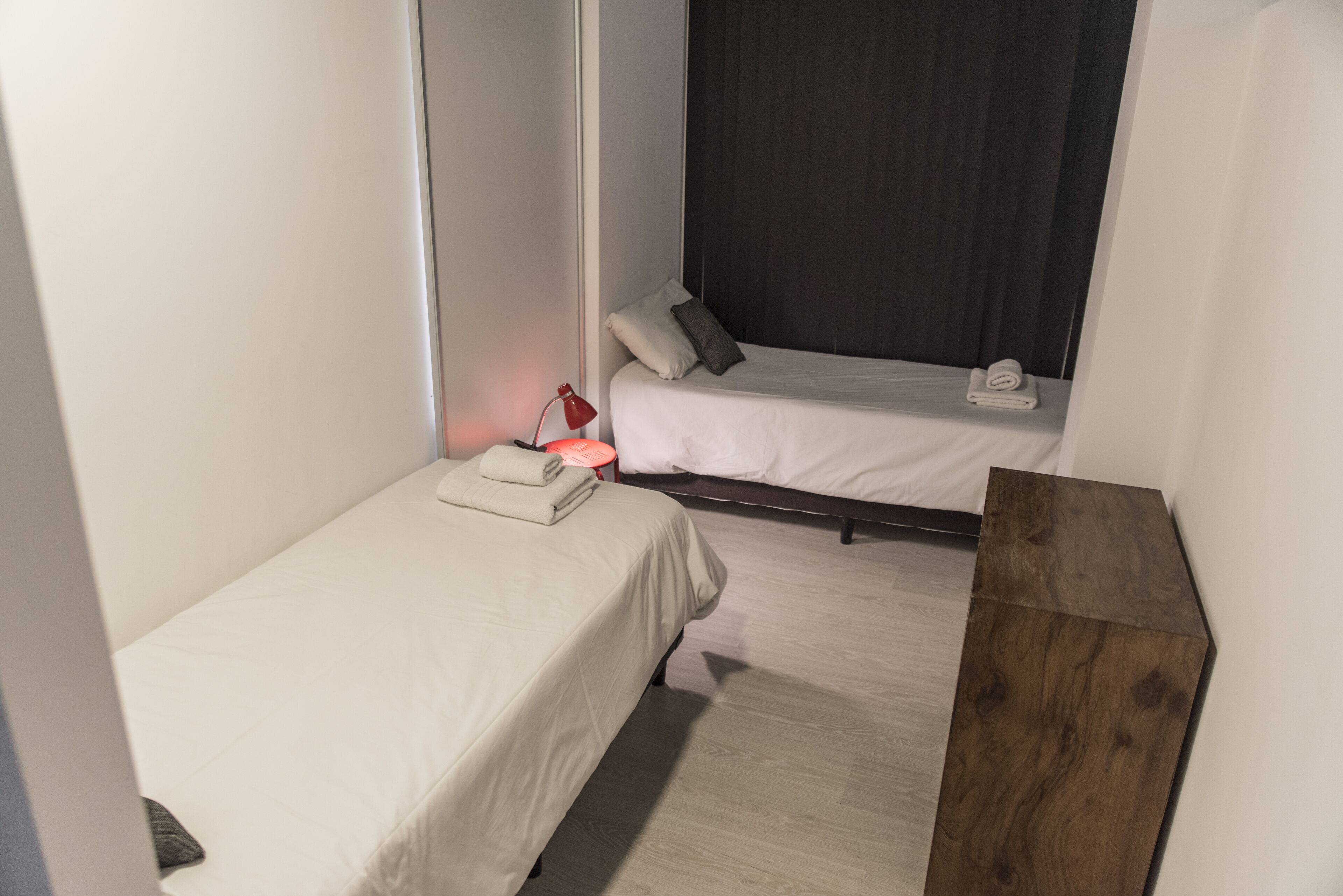A hotel room with two single beds, a wooden nightstand, and a red lamp.