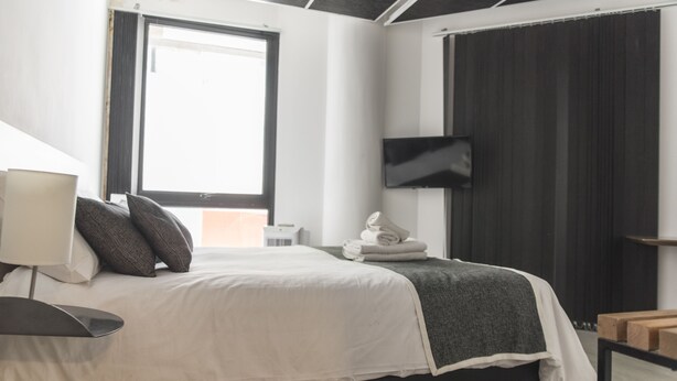 Ein modernes Schlafzimmer mit einem Bett, einem Flachbildfernseher, einem Fenster und einem Nachttisch.