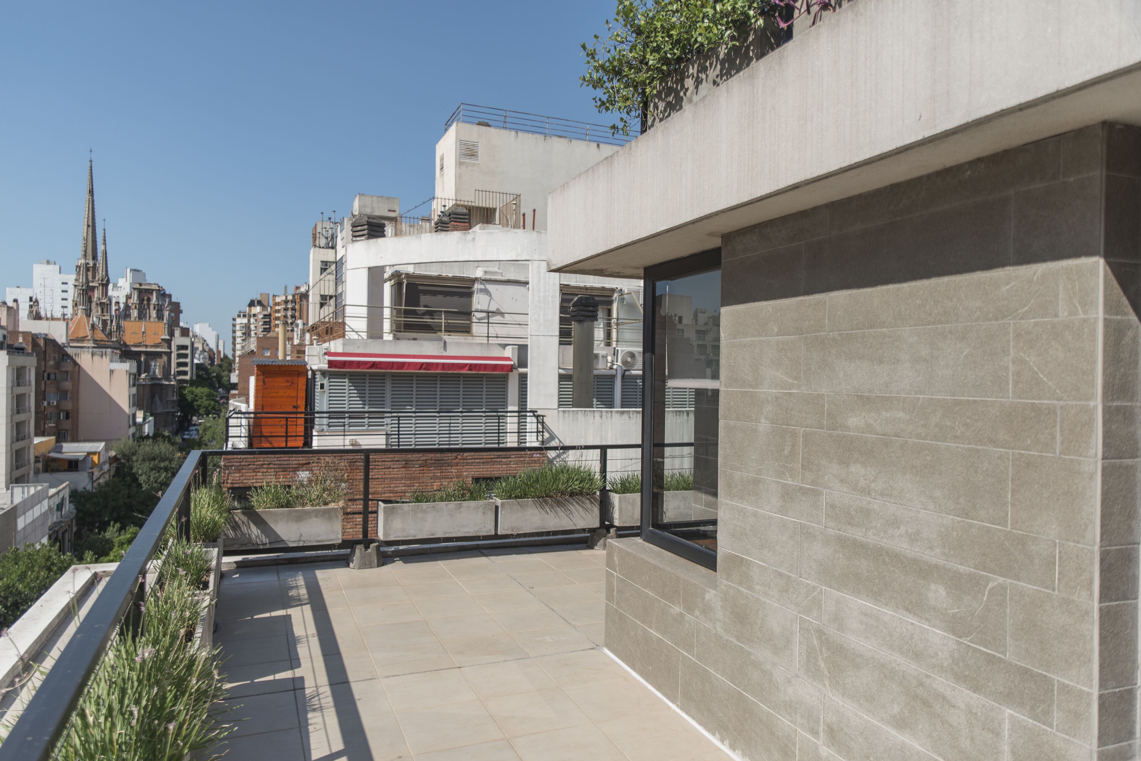 Un edificio moderno con facciata in cemento, ampie finestre e una terrazza sul tetto con piante.