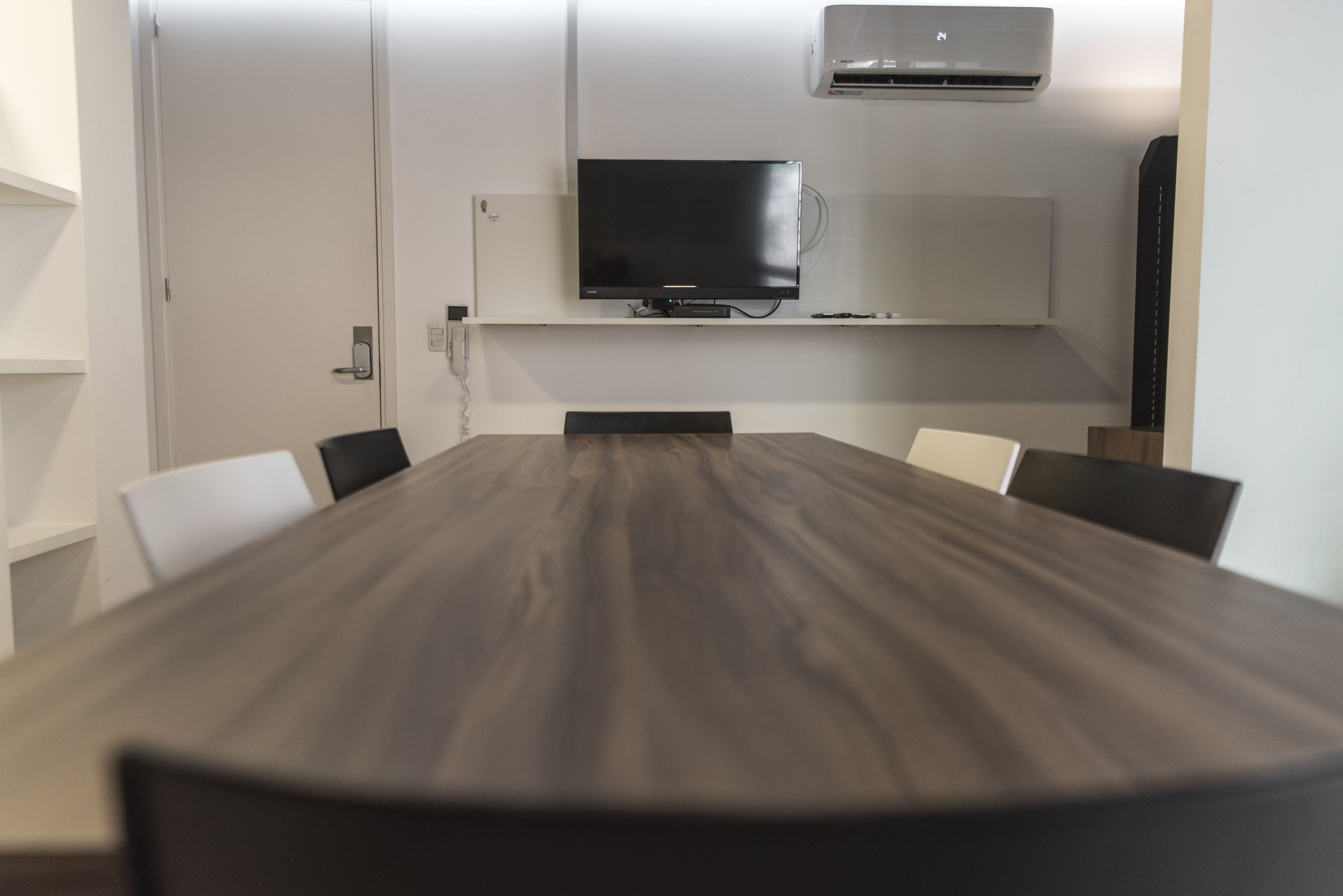 A conference room with a long table, chairs, a flat-screen TV, and an air conditioning unit on the wall.