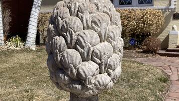A stone sculpture of a pineapple on a pedestal in a garden area.