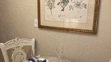 Een gedekte eettafel met borden, bestek en glazen, met een ingelijste botanische illustratie aan de muur.
