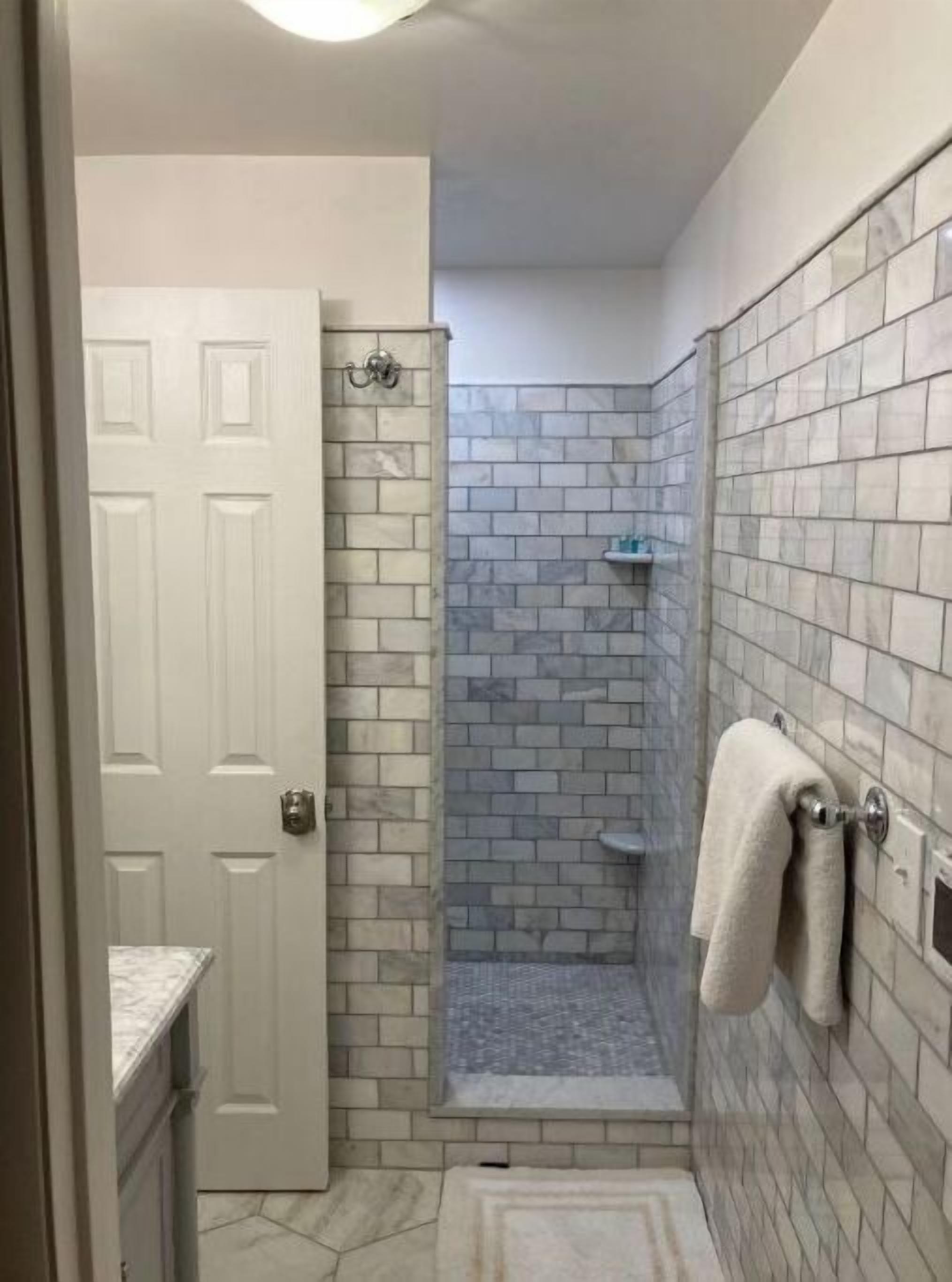 Ein Badezimmer mit Dusche, Fliesenwänden, einer weißen Tür und einem Handtuchhalter.