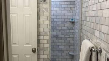 Ein Badezimmer mit Dusche, Fliesenwänden, einer weißen Tür und einem Handtuchhalter.