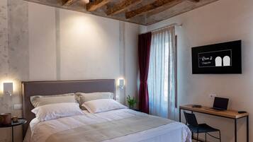 A bedroom with a bed, bedside tables, a desk, a chair, and a wall-mounted TV.