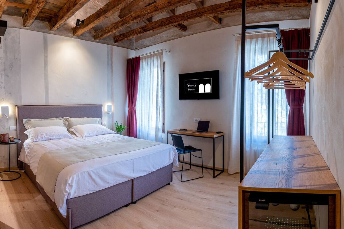 A modern hotel room with a large bed, a desk, and a TV on the wall.