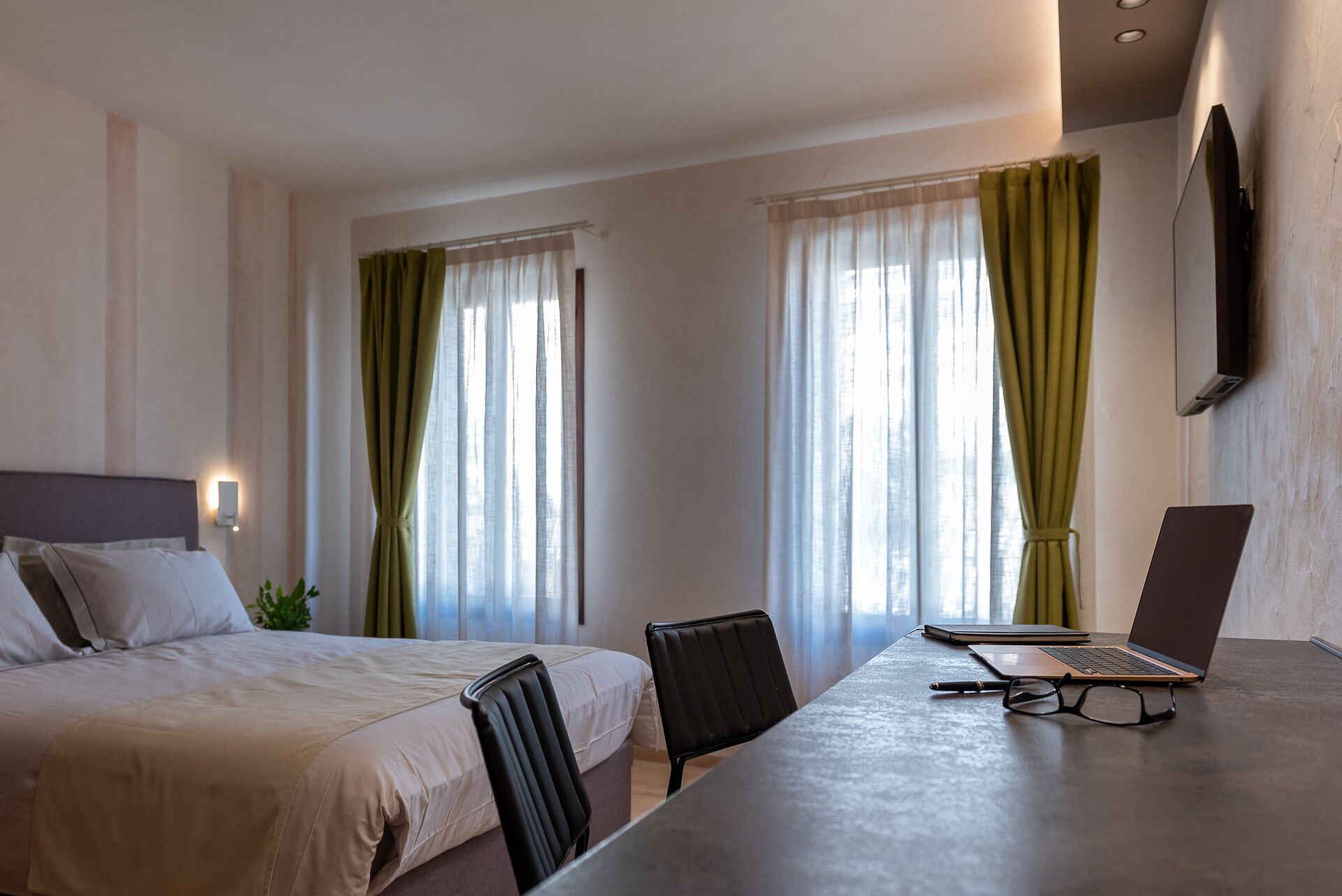 A hotel room with a bed, a desk with a laptop, and a chair.