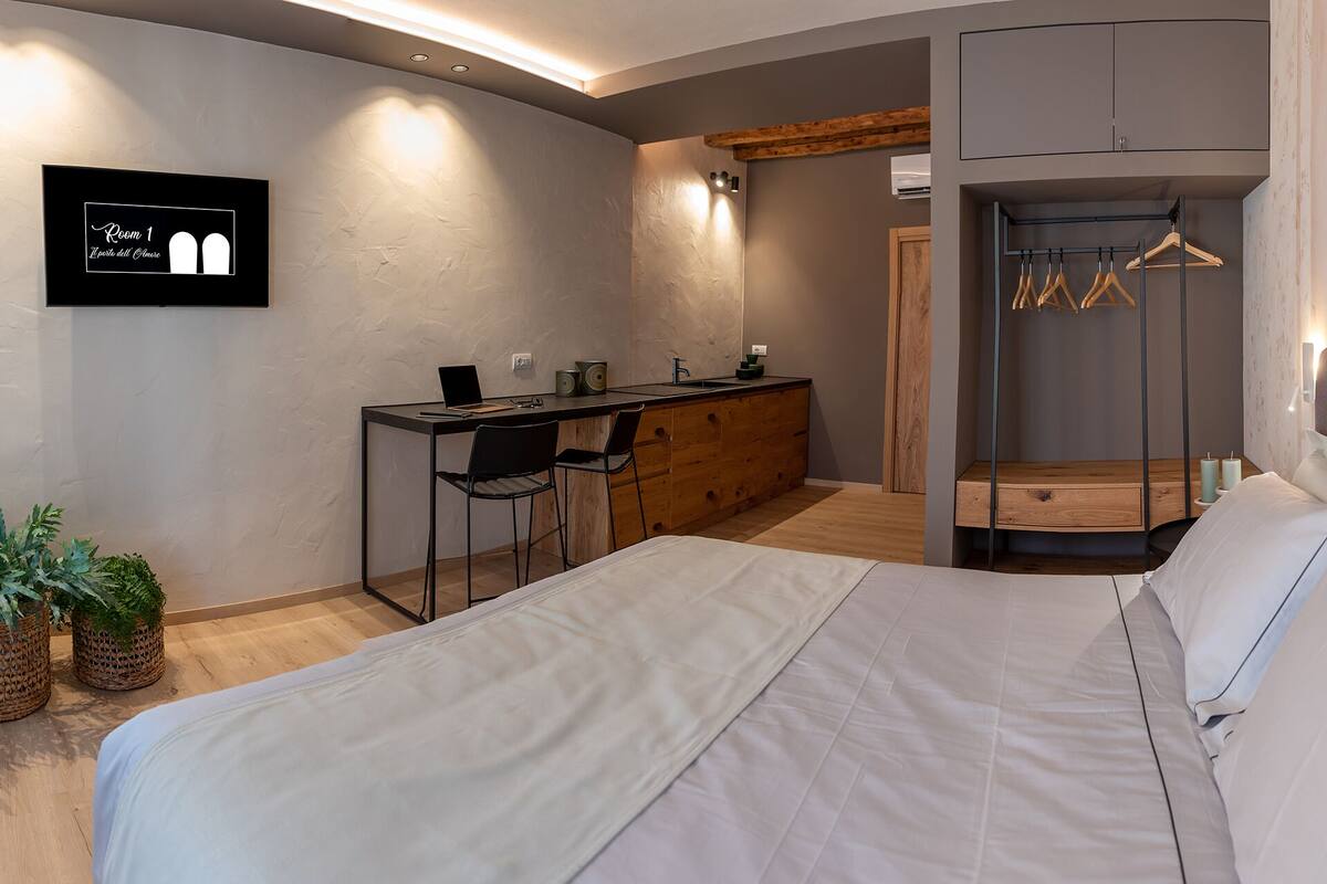 A bedroom with a bed, a desk with two chairs, a wardrobe, and a hanging clothes rack.