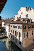 Un edificio histórico con un canal en primer plano, que presenta una fachada tradicional de ladrillo, numerosas ventanas y un pequeño puente sobre el agua.