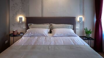 A neatly made bed with white linens, two bedside tables with lamps, a potted plant, and a window with curtains.