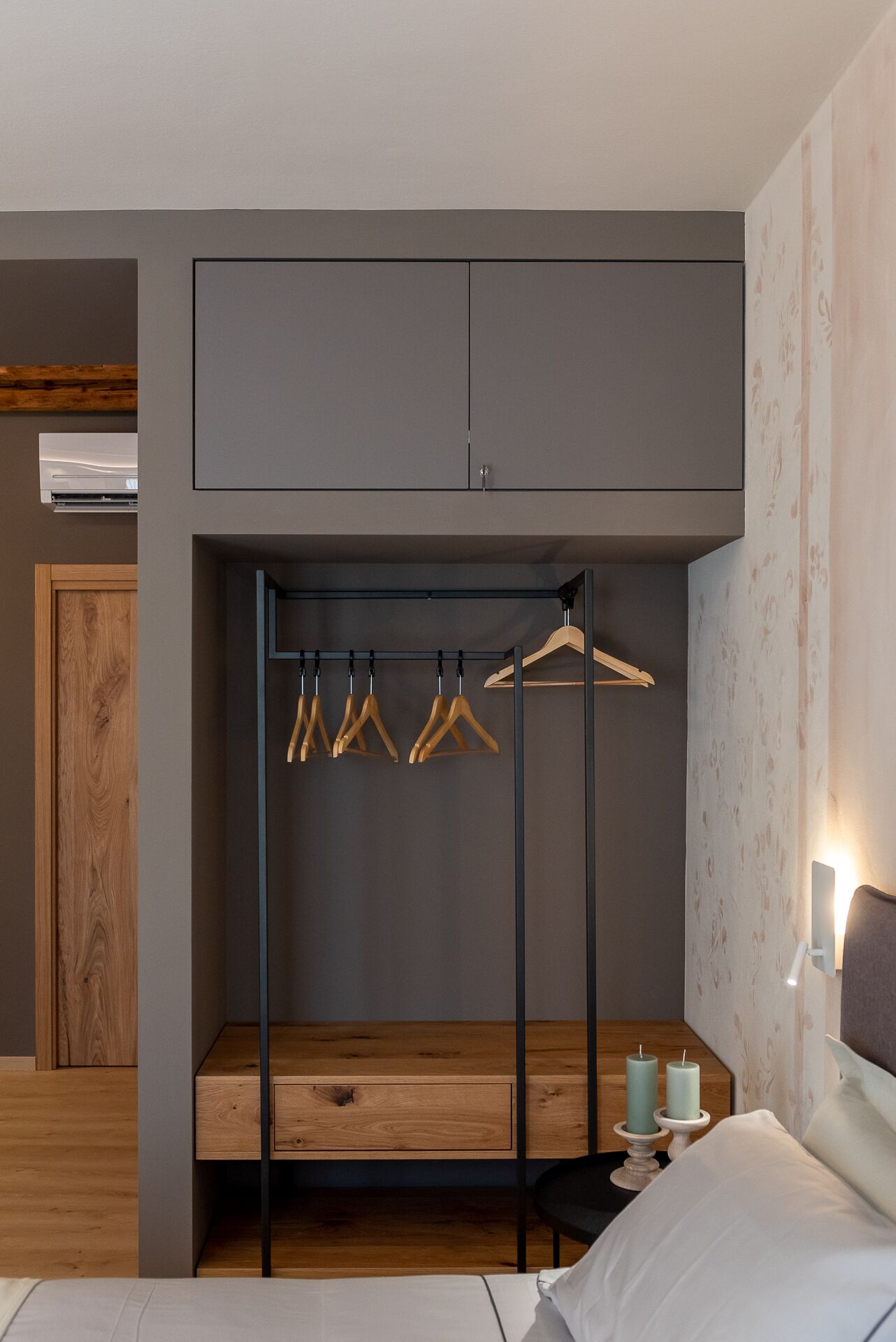 A bedroom with a built-in wardrobe, wooden bench, and hanging clothes rack.