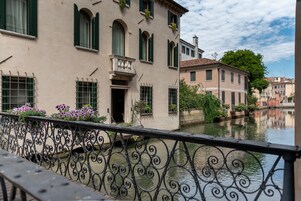 Un edificio junto a un canal con balcón, barandilla de hierro forjado y vista despejada del agua.
