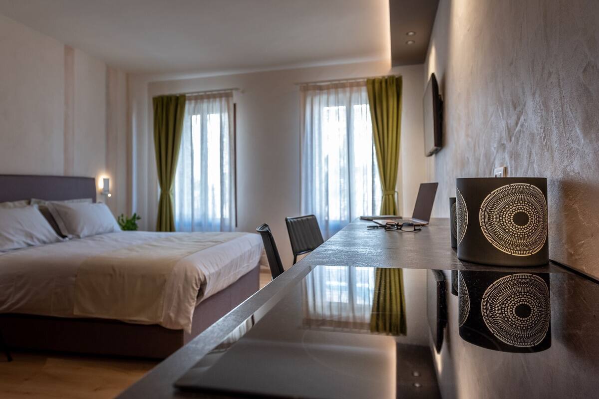 A hotel room with a bed, a desk with a laptop, a chair, and a decorative wall piece.
