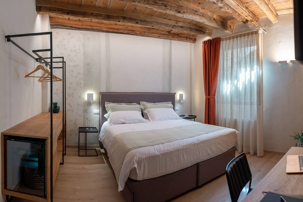 A bedroom with a bed, bedside tables, a desk with a laptop, and a wooden ceiling.