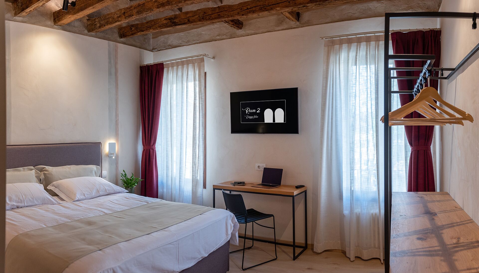 Ein Hotelzimmer mit einem Bett, einem Schreibtisch mit Laptop, einem Fernseher und einem Kleiderständer.