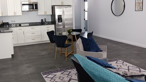 Een moderne keuken met witte kasten, roestvrijstalen apparatuur en een eethoek met een zwarte bank en een kamerbreed tapijt.