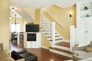 A living room with a staircase, a television, and a dining area. - The Savannah: 2BR + Loft Townhome Sleeps 8 | Pool, Hot Tub, Free Golf, Near Lake Michigan (Holland)